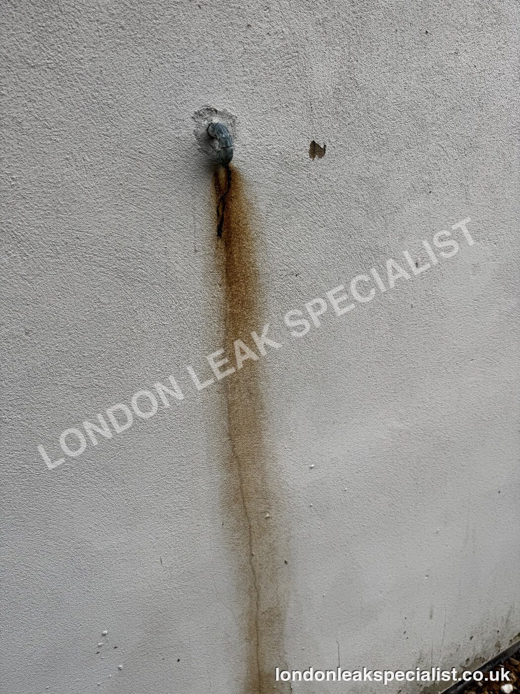 A long rust-coloured streak running down a rendered wall from a small pipe outlet near the top
