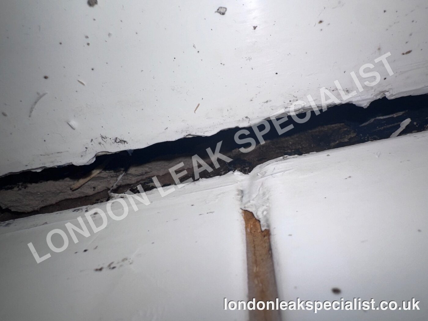 An open joint at the edge of a shower tray with stained timber visible beneath, in a flat in Kentish Town, north London