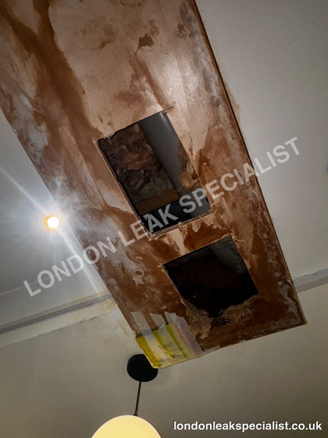 A boxed-in section of ceiling with two square inspection openings cut into it and water staining around them