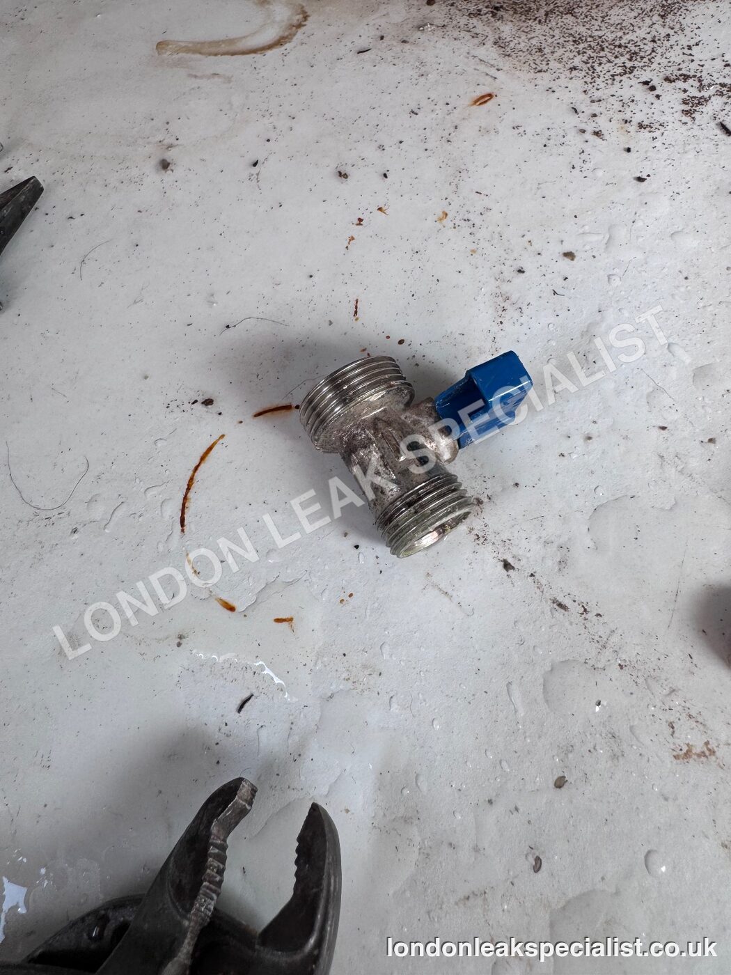 A chrome compression isolation valve with a blue lever lying on a floor after being removed